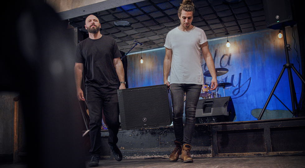 Two band members carrying Thumpv4 subwoofer by handles.